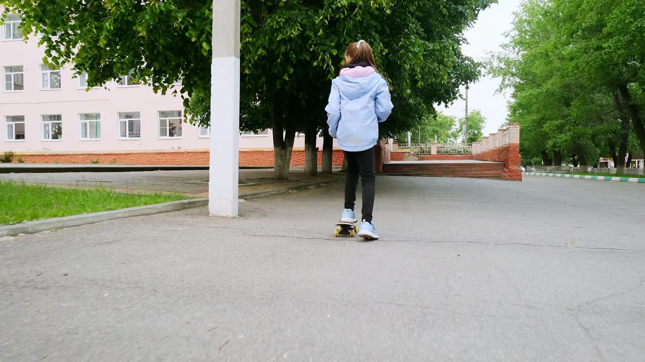 小女孩在柏油路上学习滑板。快乐的女孩在夏天骑滑冰在街上视频素材