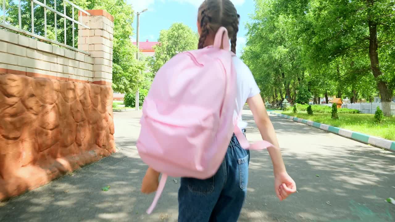 回到学校。一个背着背包的小女孩沿着马路穿过校园往学校跑。教育孩子的理念。一个背着背向背包的小孩跑向学校视频素材