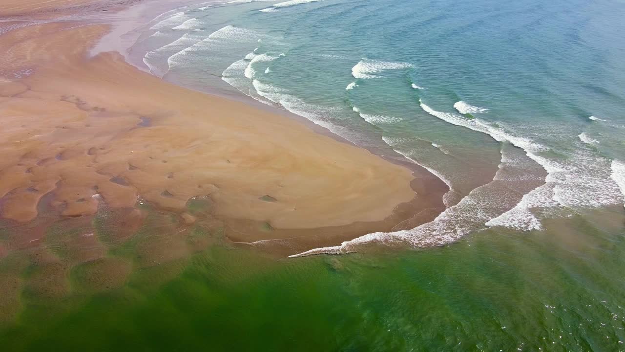 退潮时，海浪在沙滩上形成图案，展示了海岸线上的水和陆地的混合。视频素材