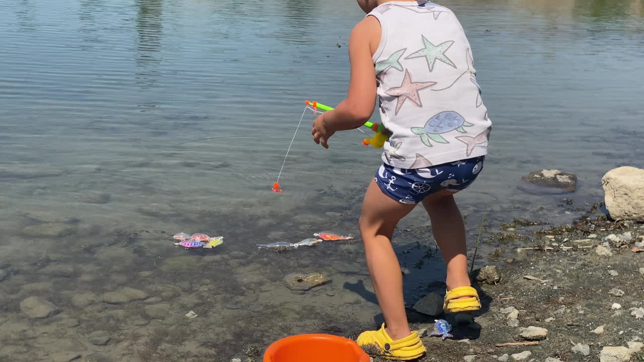 快乐的小渔夫在夏天玩着玩具鱼竿在湖里捉玩具鱼视频素材