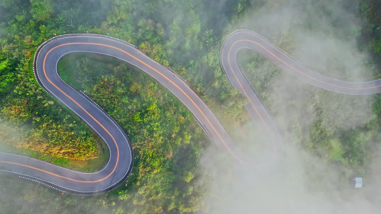 清晨森林中的乡村公路鸟瞰图。无人驾驶飞机飞过乡村公路，在山间有雾。泰国南省的标志性旅游景点视频下载