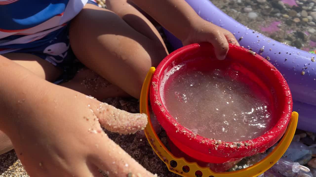 小孩子在沙滩上的充气儿童泳池边玩耍。小男孩穿着防晒衬衫。孩子们暑假。视频下载