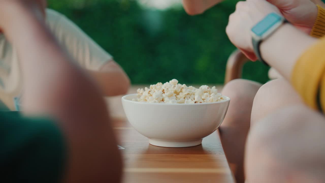 一群亚洲年轻人在聚会上用一碗爆米花当零食玩纸牌游戏。视频素材