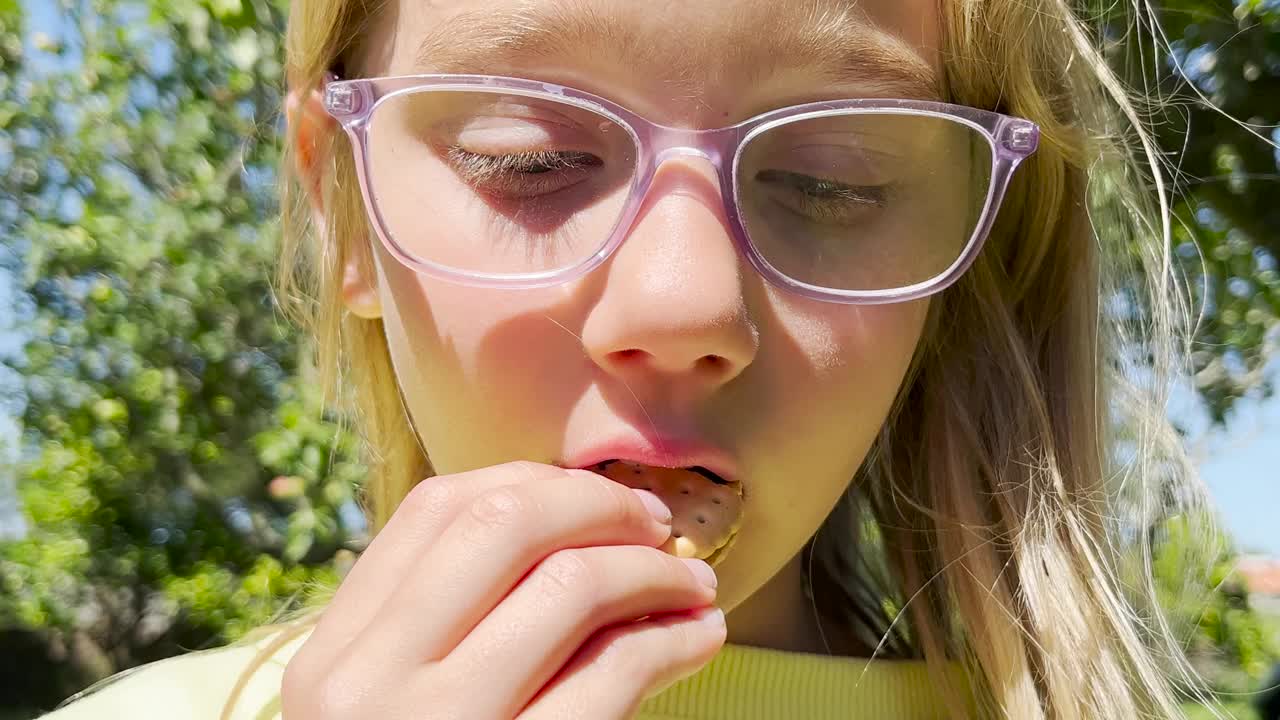 一个8岁的金发女孩在户外吃巧克力夹心饼干。这个孩子正在吃饼干视频下载