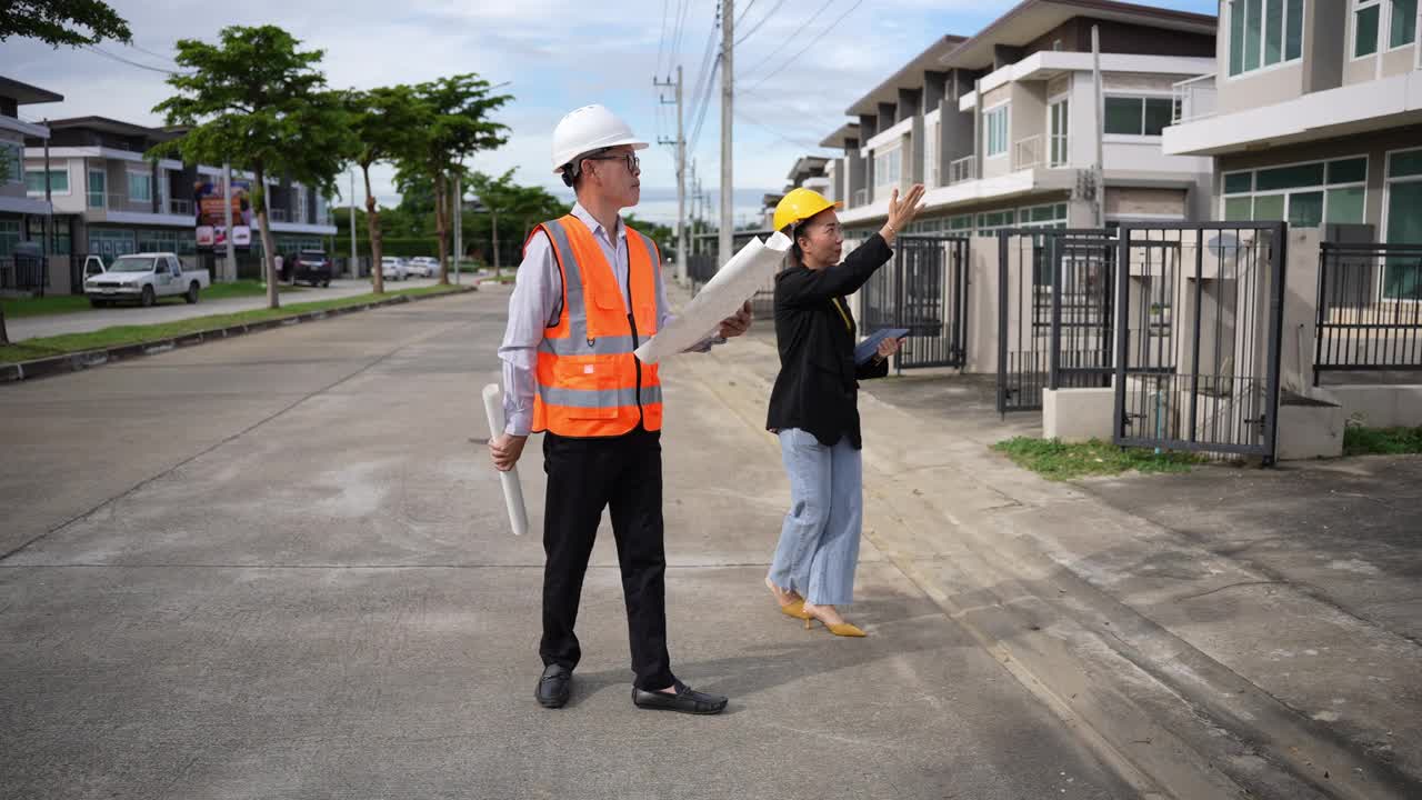 亚洲房地产商视察住宅项目年轻的建筑师夫妇在住宅建筑工地讨论和观看蓝图。视频下载