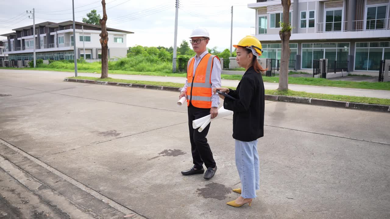 亚洲房地产商视察住宅项目年轻的建筑师夫妇在住宅建筑工地讨论和观看蓝图。视频下载