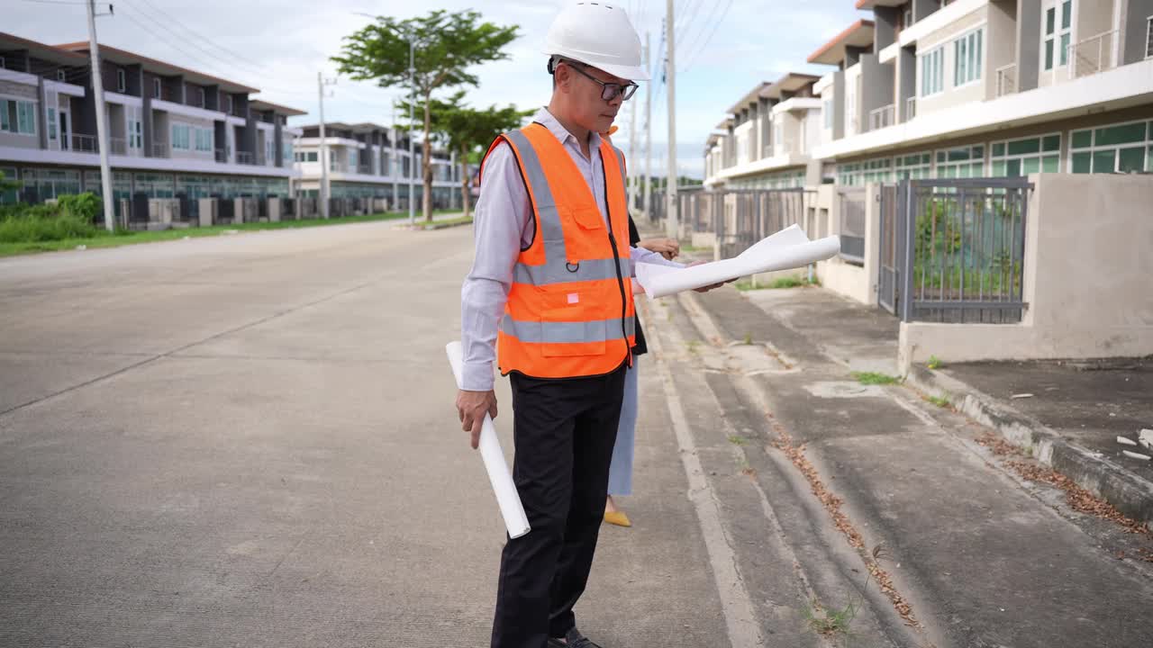 亚洲房地产商视察住宅项目年轻的建筑师夫妇在住宅建筑工地讨论和观看蓝图。视频下载