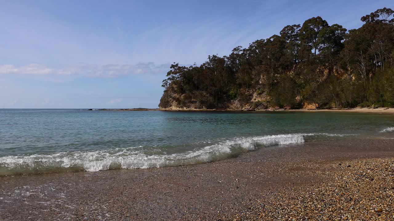 田园诗般的海岸海湾，海浪在蔚蓝的阳光下冲刷着长长的卵石海岸线。视频素材