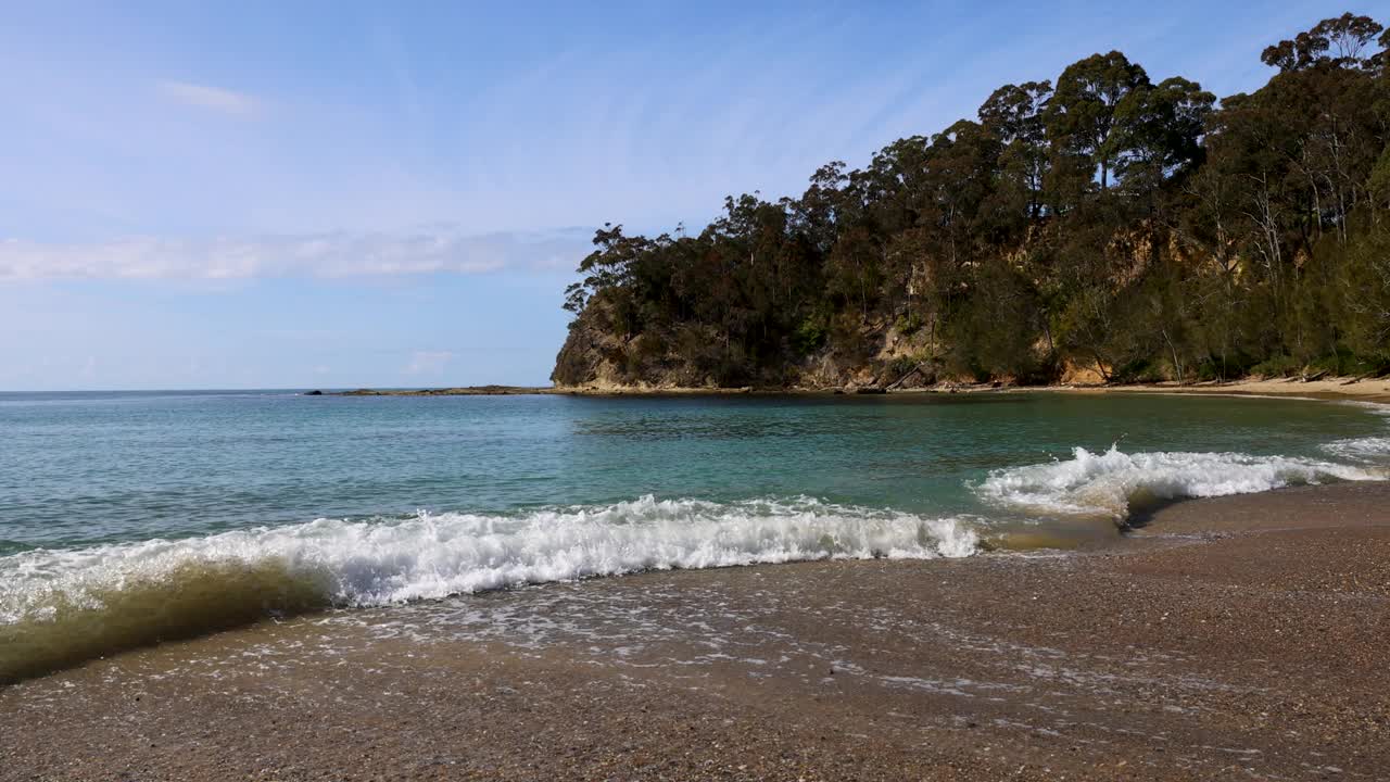 田园诗般的海岸海湾，海浪在蔚蓝的阳光下冲刷着长长的卵石海岸线。视频下载