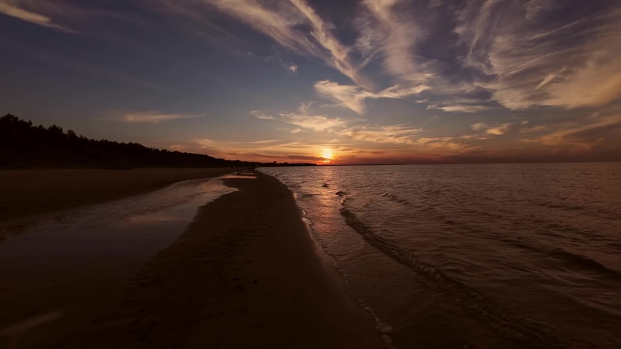 在宁静的海滩上欣赏日落的壮丽景色，柔和的海浪和充满戏剧性云的天空，创造了一个宁静而迷人的海岸场景。视频素材