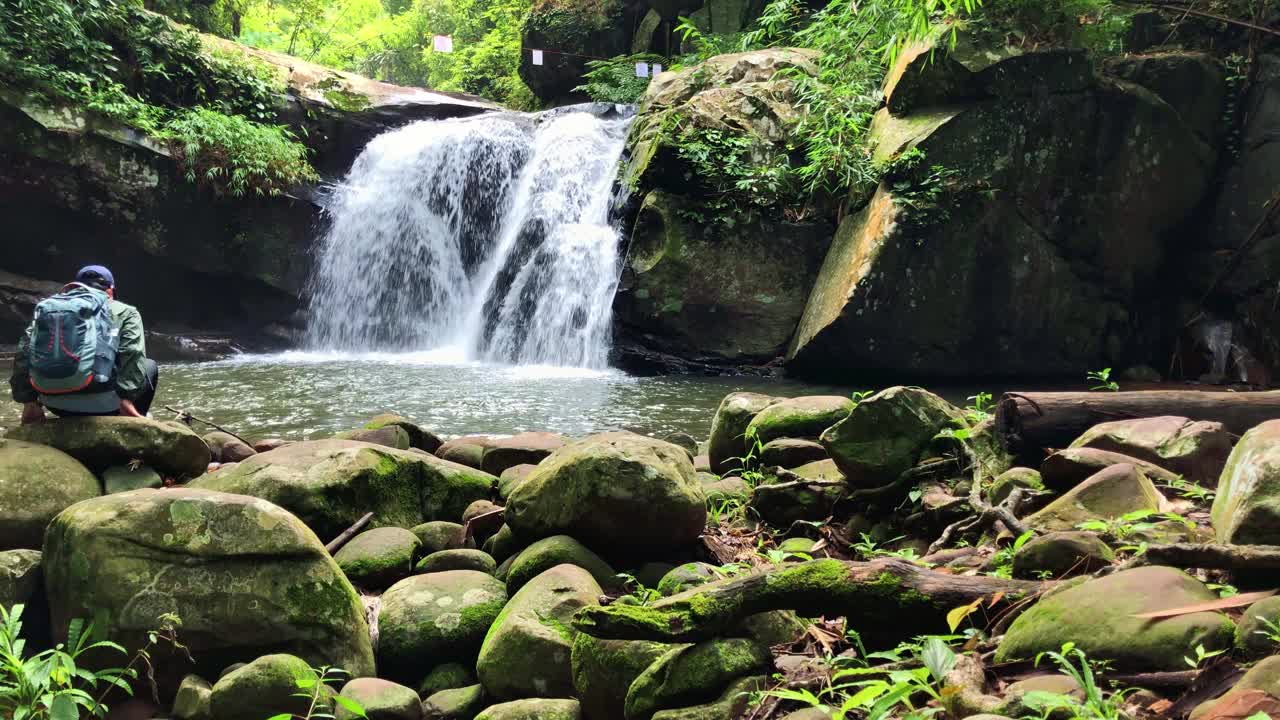 步道上的雨林瀑布和背包中的冒险家徒步旅行者享受热带瀑布视频素材