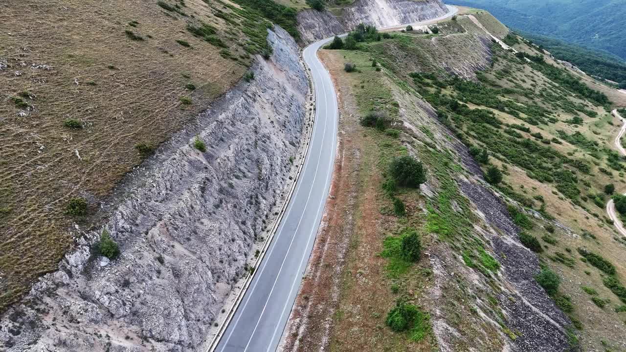 柔软的云下蜿蜒的山路，一辆汽车在绿色的山丘上行驶视频素材