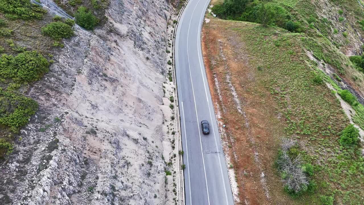 柔软的云下蜿蜒的山路，一辆汽车在绿色的山丘上行驶视频素材