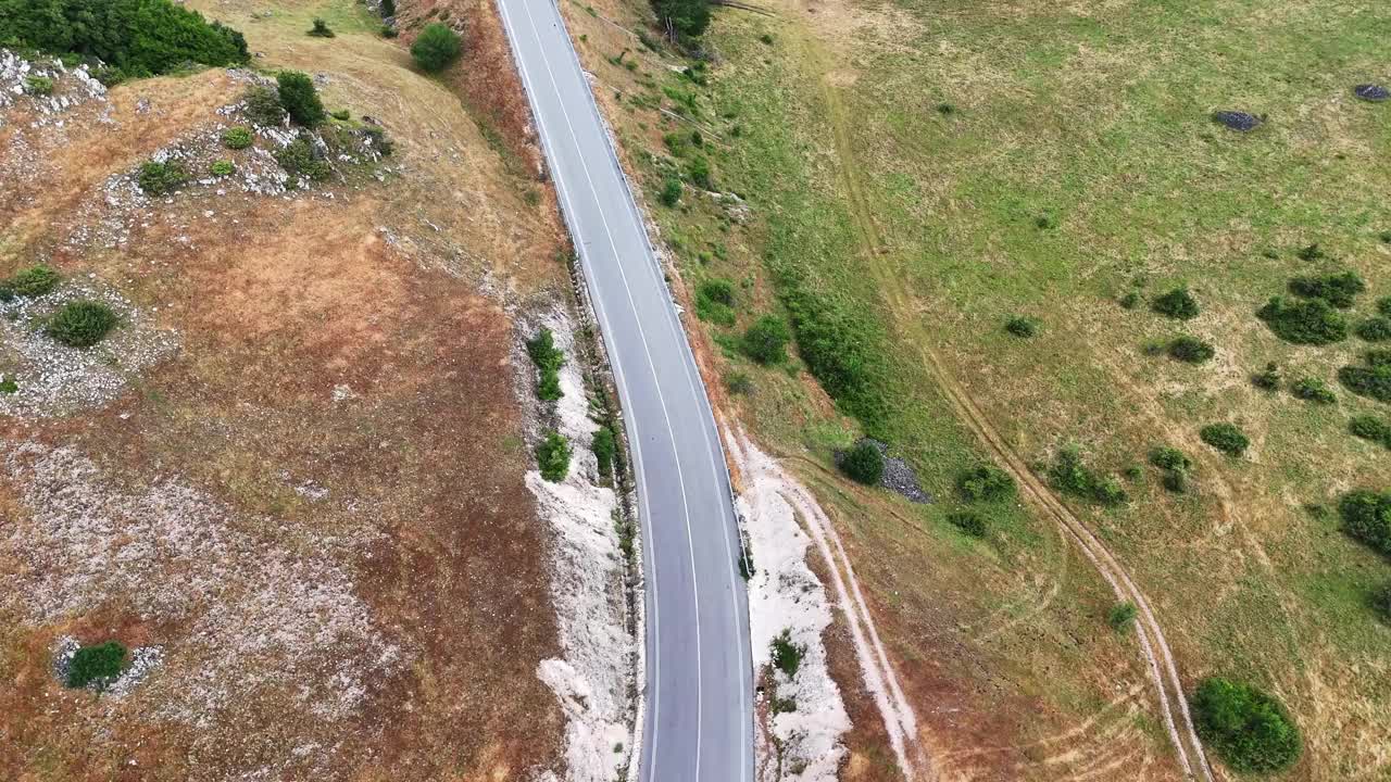 柔软的云下蜿蜒的山路，一辆汽车在绿色的山丘上行驶视频素材