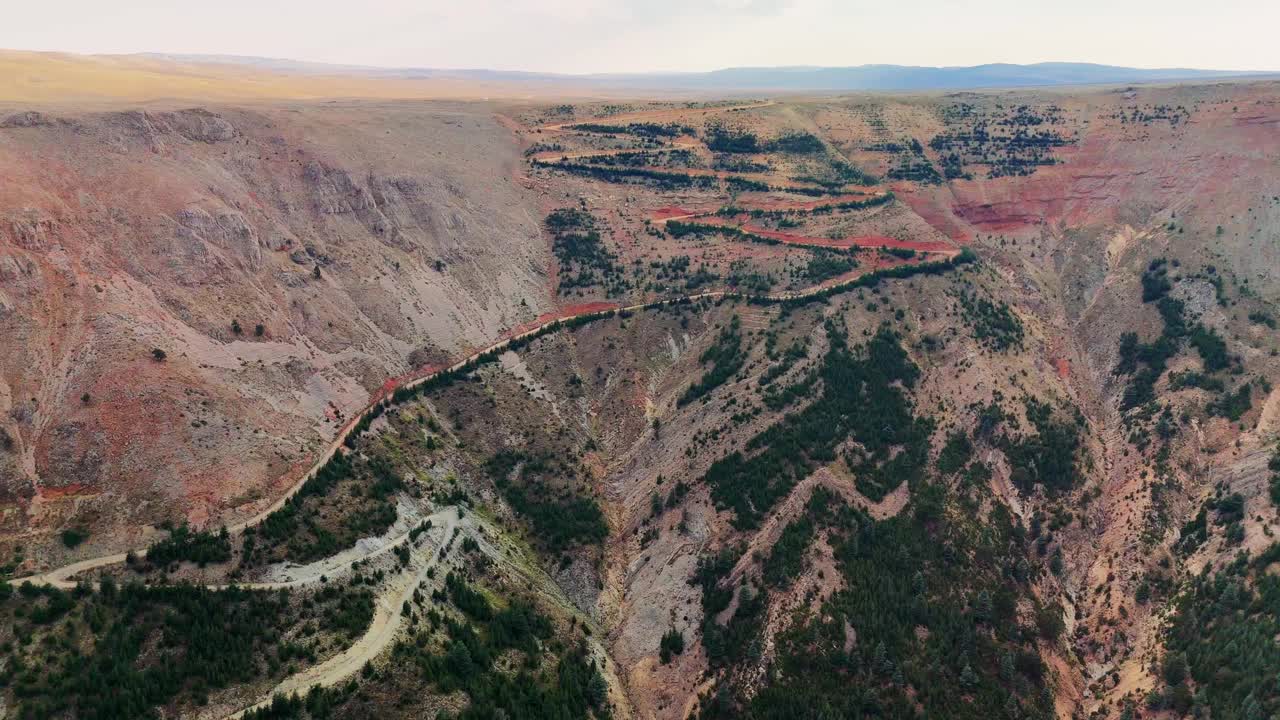 蜿蜒的道路蜿蜒穿过充满活力的沙漠峡谷，在明亮的天空下揭示出令人惊叹的岩层和丰富多彩的地质层视频下载