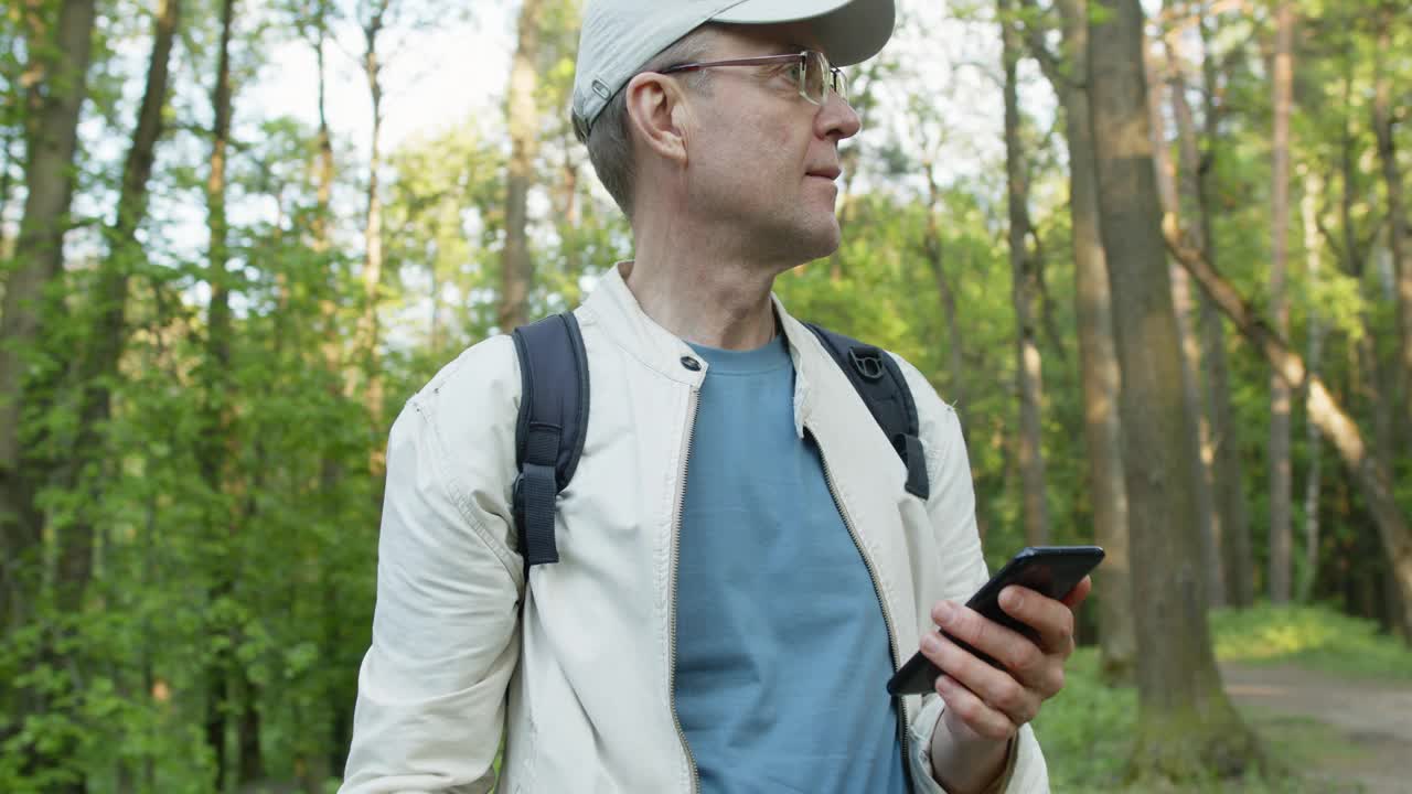 老人带着智能手机在森林里徒步旅行视频下载