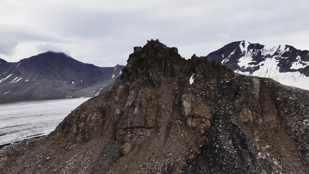 一座岩石山，周围是一片没有生命的田野，周围撒满了火山灰，旁边是一个巨大的冰川舌。冰岛景观鸟瞰图视频下载