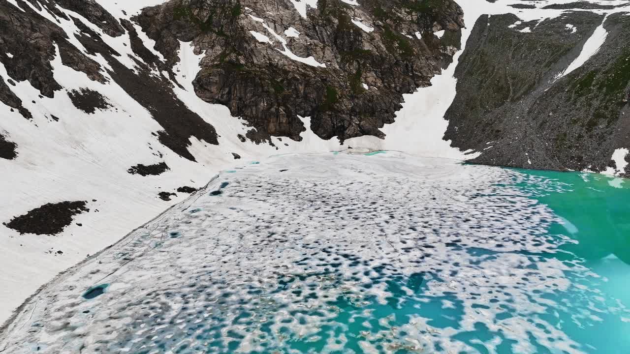 被雪崩袭击的高山湖泊当地的高原湖泊，在阴天被陡峭的山峰包围。鸟瞰图视频下载