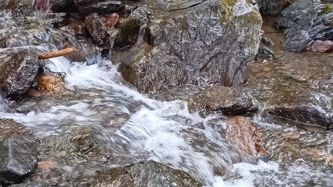 在一个阳光明媚的夏日早晨，一条小瀑布在湍急的溪流中从山上流下，弯曲在床上的石头周围。视频素材