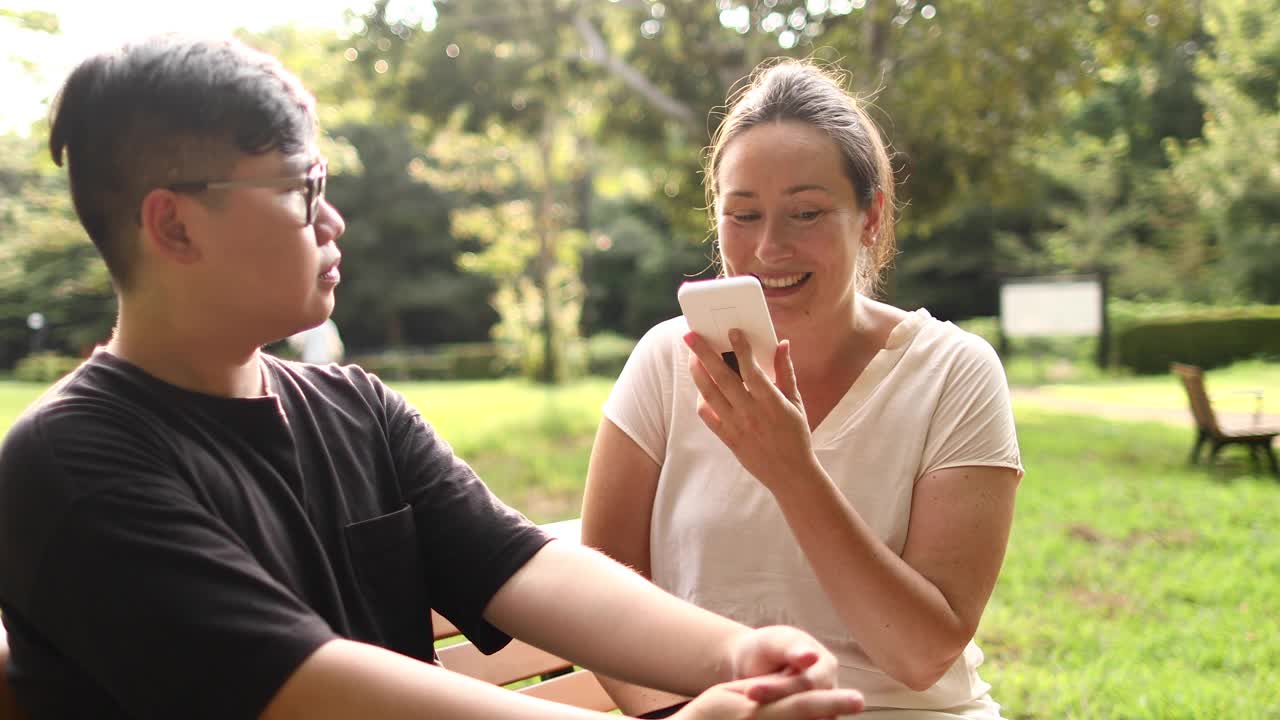 一名亚洲男子和一名白人女子在公园里使用带有语音识别功能的语言翻译功能交谈。视频素材