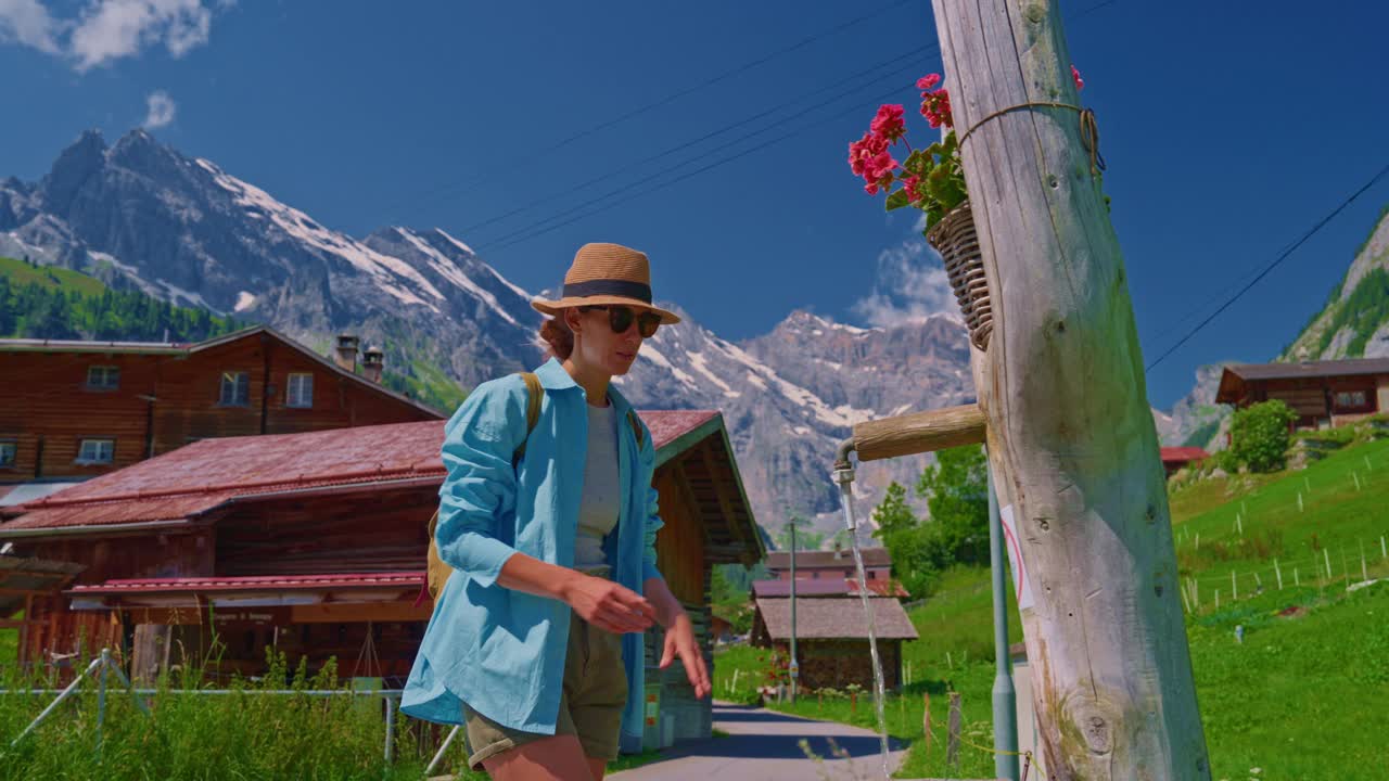 在风景如画的瑞士阿尔卑斯山徒步旅行后，背着背包的女孩喝着饮水机里的水视频下载