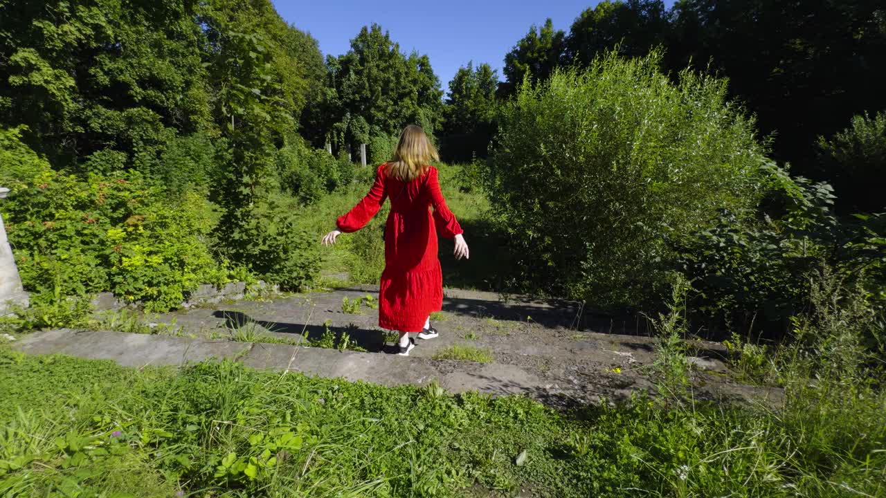 在废弃的公园里，穿红裙子的女人跑下杂草丛生的石阶视频下载