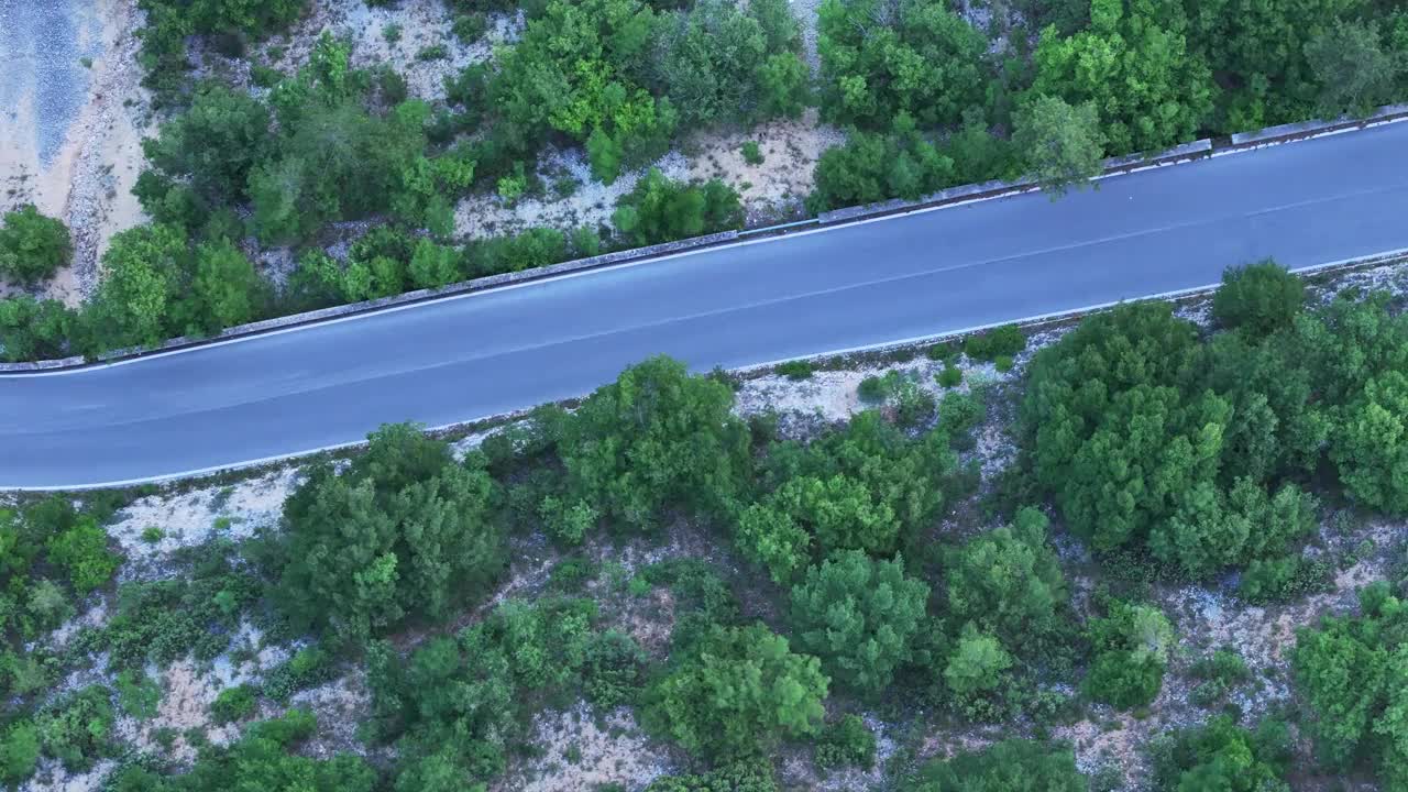 在阳光明媚的日子里，蜿蜒的乡村道路被郁郁葱葱的绿色森林包围视频下载