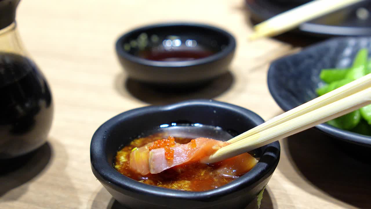 在一家日本餐馆里，一个亚洲女孩开心地用筷子夹着三文鱼刺身。视频素材