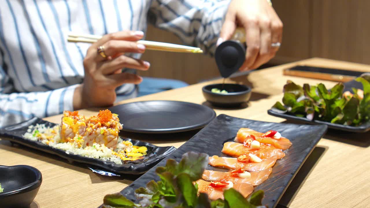 亚洲女孩和家人在日本餐厅为寿司倒蘸酱。视频素材