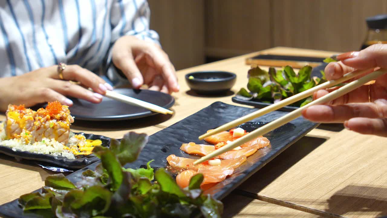 在一家日本餐馆里，一个亚洲女孩开心地用筷子夹着三文鱼刺身。视频素材