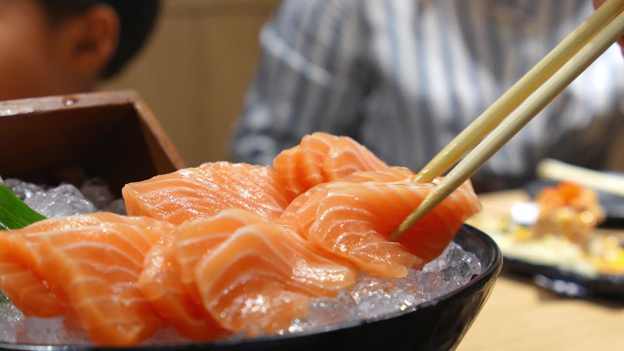 在一家日本餐馆里，一个亚洲女孩开心地用筷子夹着三文鱼刺身。视频素材