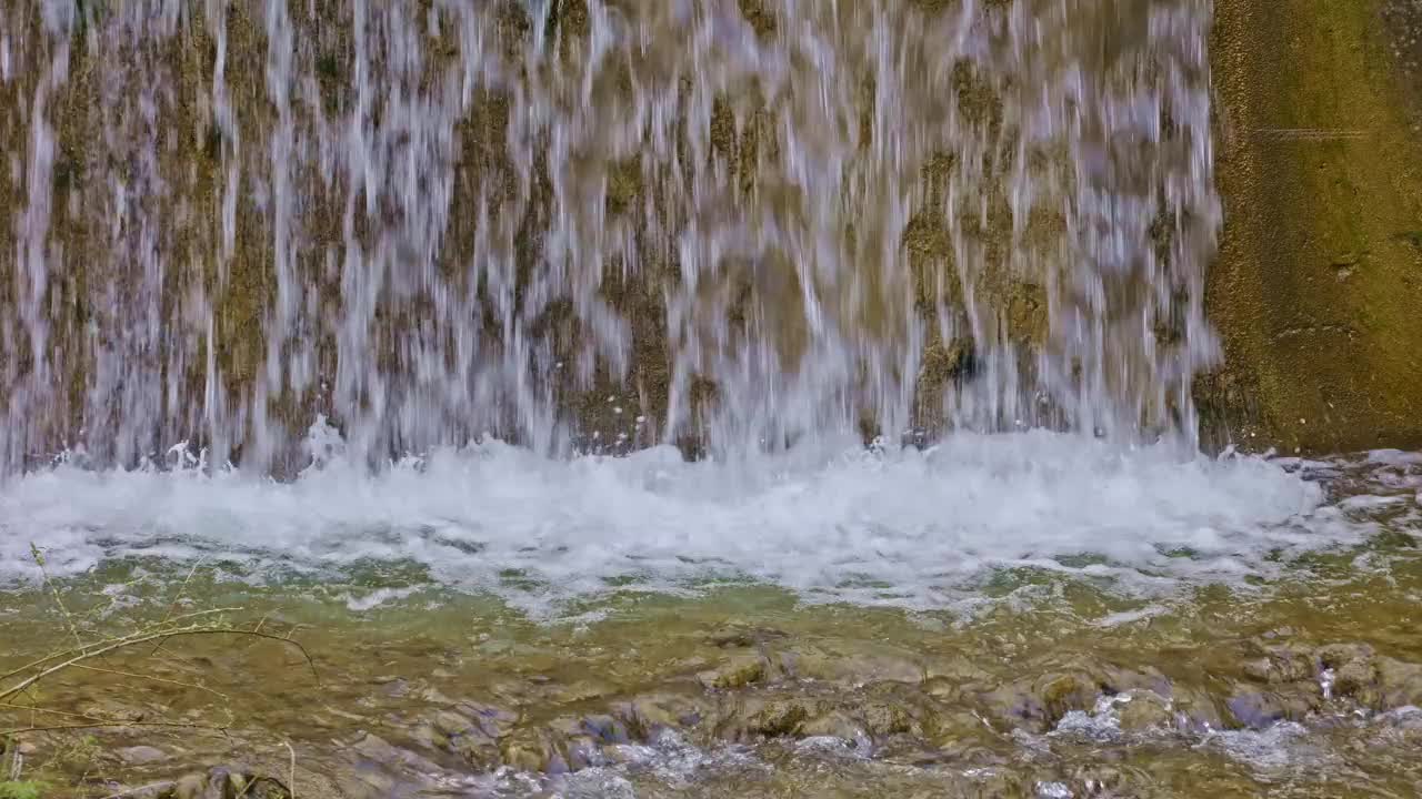 水从人造瀑布倾泻而下，特写。河水绕着石头流动。内瓦尔登州贝肯里德附近的Traeschlibach视频下载