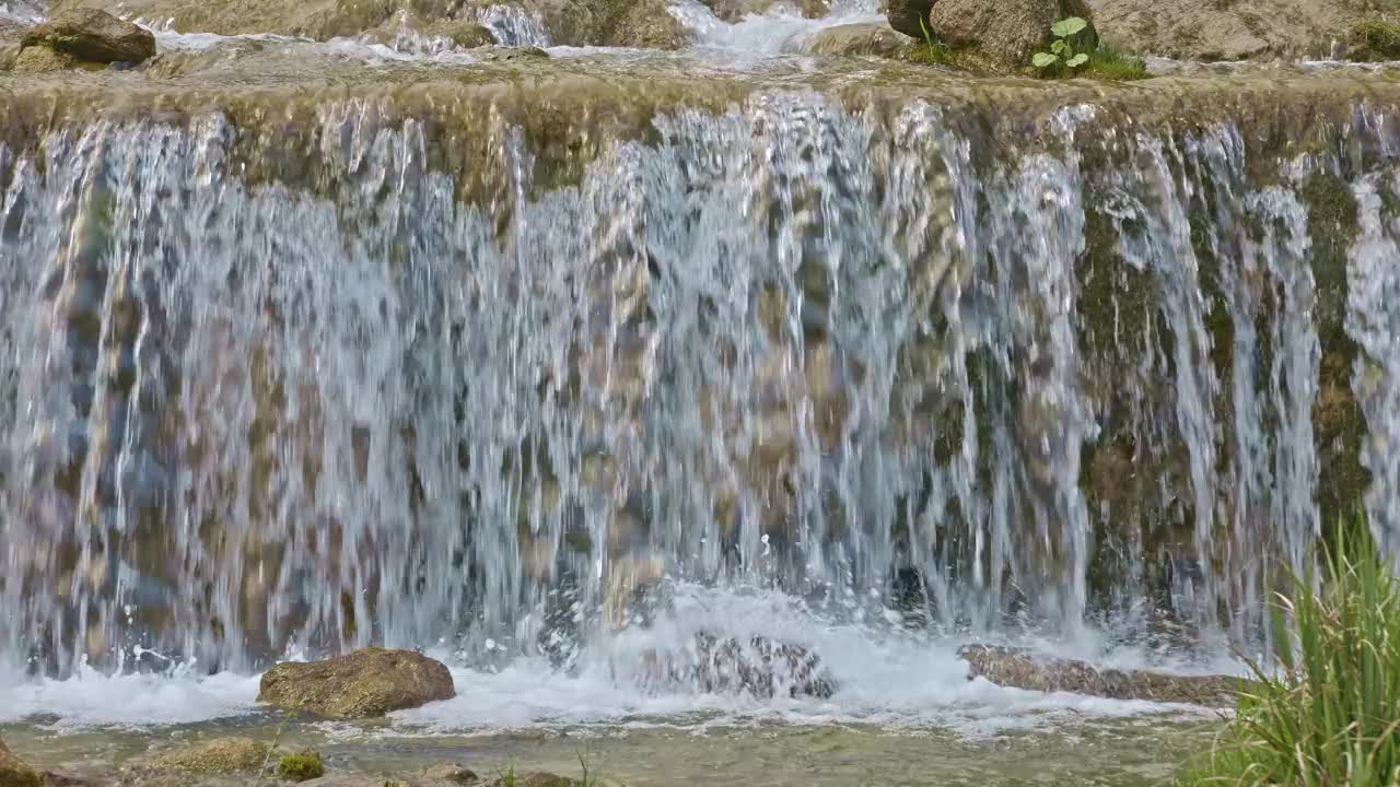 水从人造瀑布倾泻而下，特写。河水绕着石头流动。内瓦尔登州贝肯里德附近的Traeschlibach视频下载