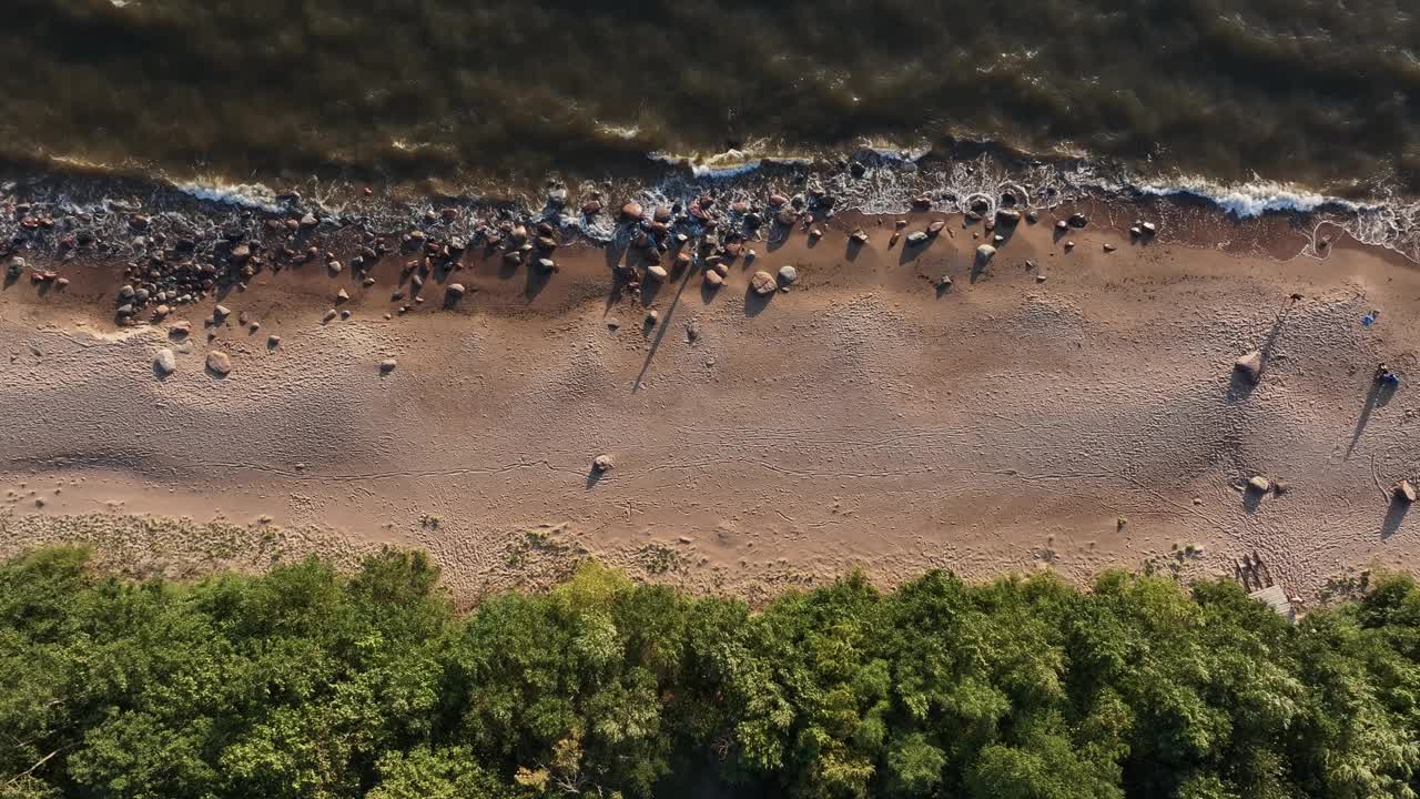 沙滩的海岸，海浪冲刷着沙滩，岩石散落在水边视频素材