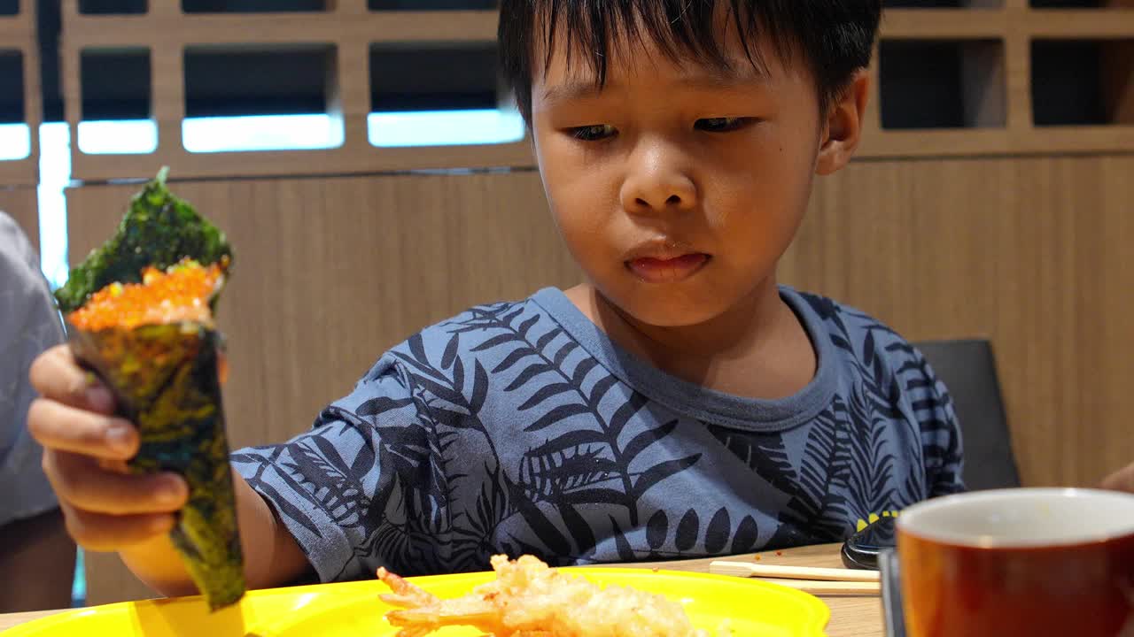 亚洲男孩在日本餐厅吃着美味的蟹肉棒寿司。视频素材