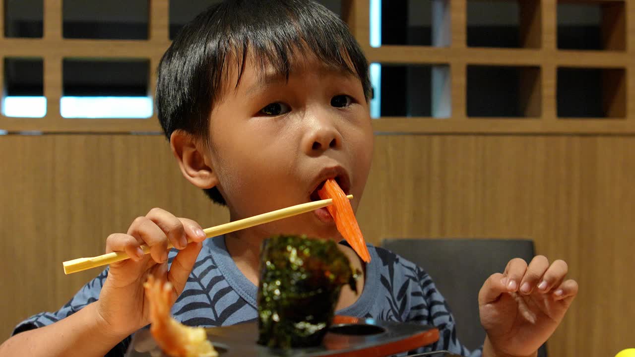 亚洲男孩在日本餐厅吃着美味的蟹肉棒寿司。视频下载