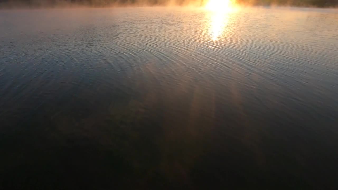 空中-飞越大海，倾斜到半岛上粉红色的日落。美丽的涟漪水与平静的波浪反射在它的表面上五颜六色的夕阳视频下载