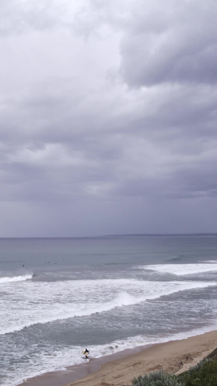 在一个暴风雨的日子里，在澳大利亚的第13海滩，一名冲浪运动员在引人注目的云层下涉水冲浪。视频素材