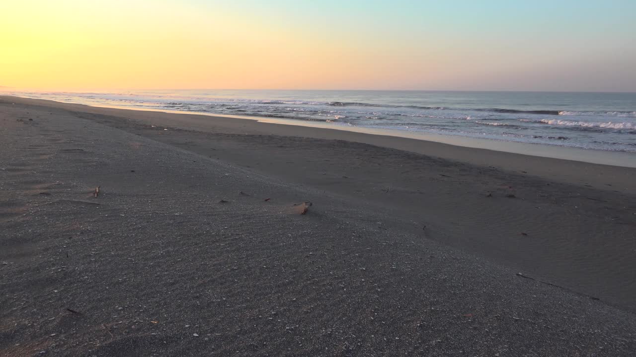 在一片空旷的海滩上，五彩缤纷的日出时，海浪涌向岸边视频素材