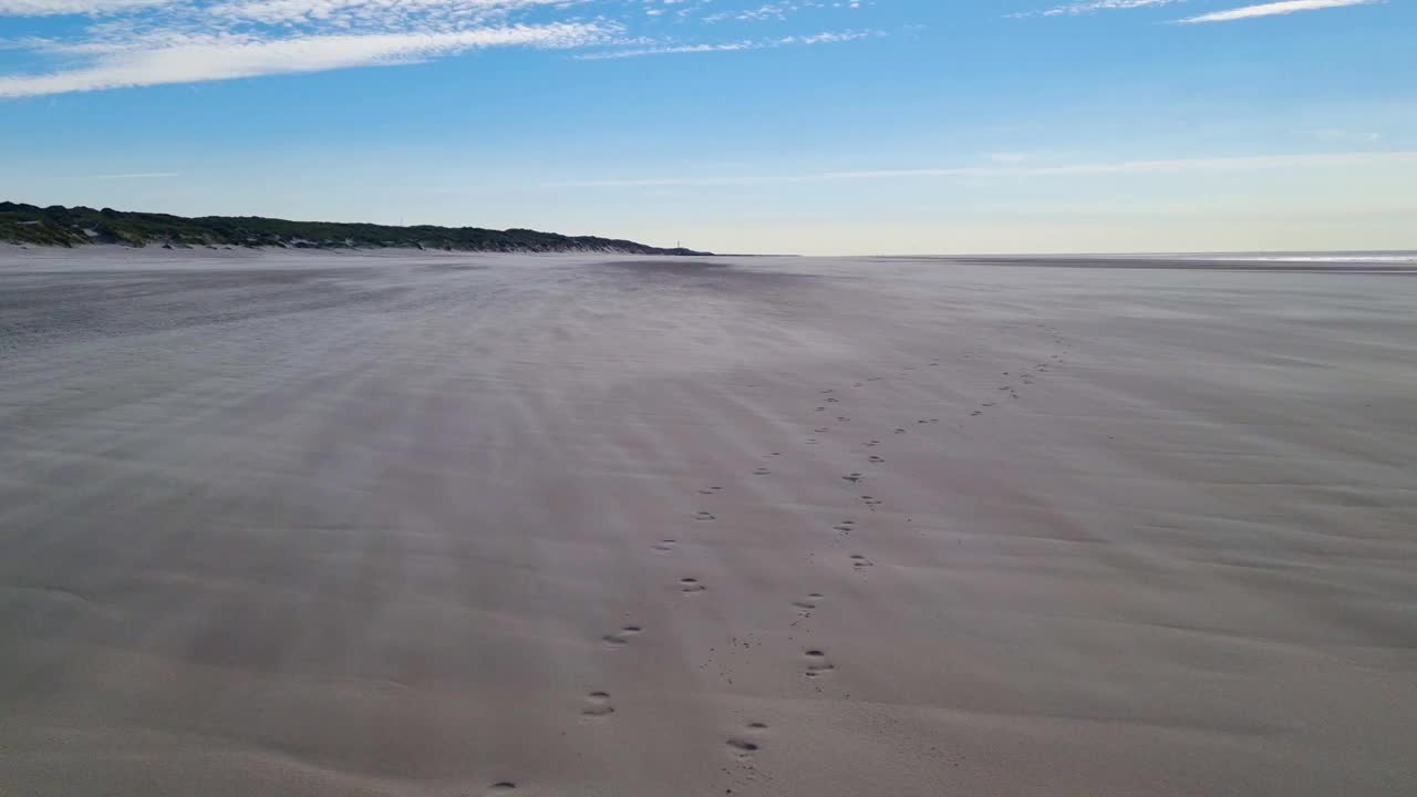 宁静的海滩场景，在蓝天下的脚印通向遥远的地平线视频下载