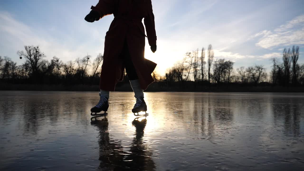 冰天雪地里，穿着花样滑冰鞋的女子在湖面上滑行。日落时分，滑冰者的女脚在结冰的河上滑冰。耀眼的阳光反射在冰面上。冬季积极休闲。缓慢的莫视频下载