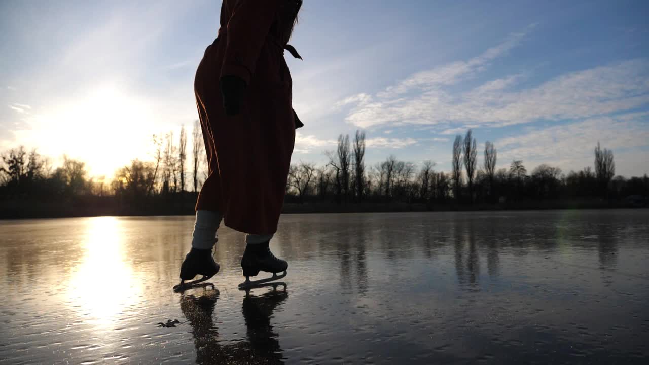 冰天雪地里，穿着花样滑冰鞋的女子在湖面上滑行。日落时分，滑冰者的女脚在结冰的河上滑冰。耀眼的阳光反射在冰面上。冬季积极休闲。缓慢的莫视频素材