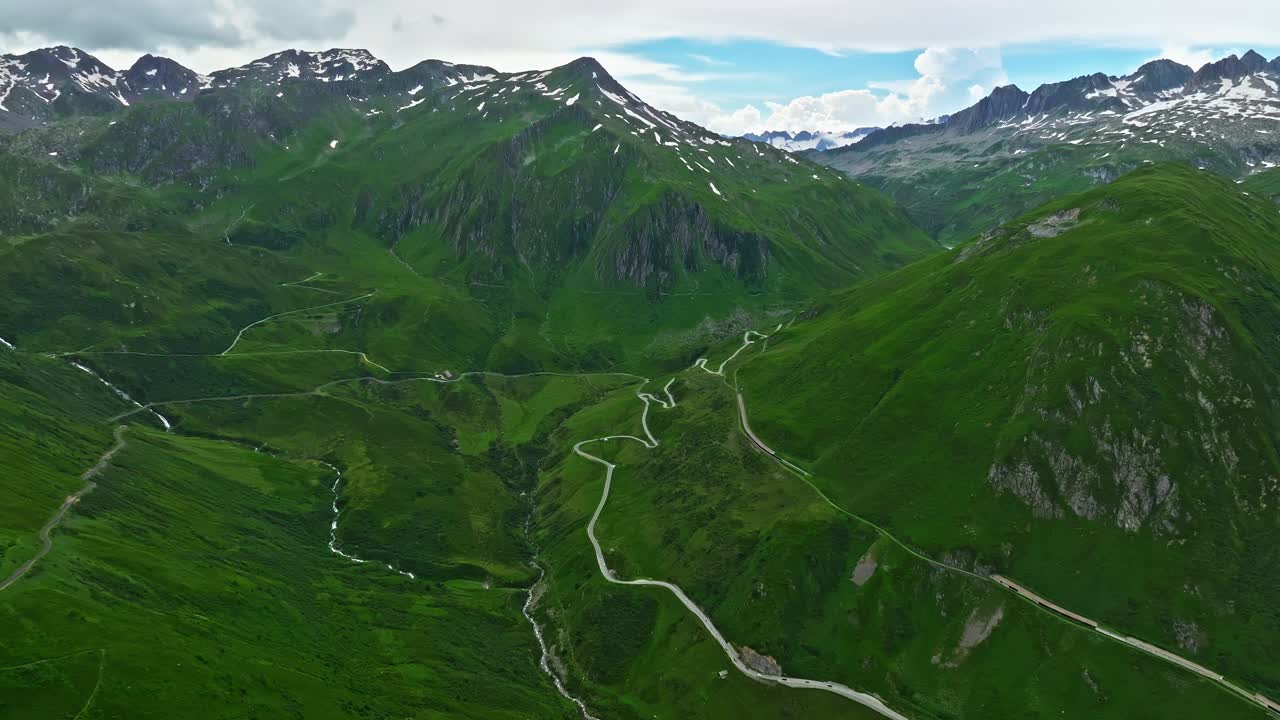 鸟瞰图，游客在公路旅行中穿越瑞士山脉，沿着发夹转弯行驶。空中无人机拍摄蜿蜒的山路穿过草地。瑞士阿尔卑斯山蜿蜒曲折的道路视频下载