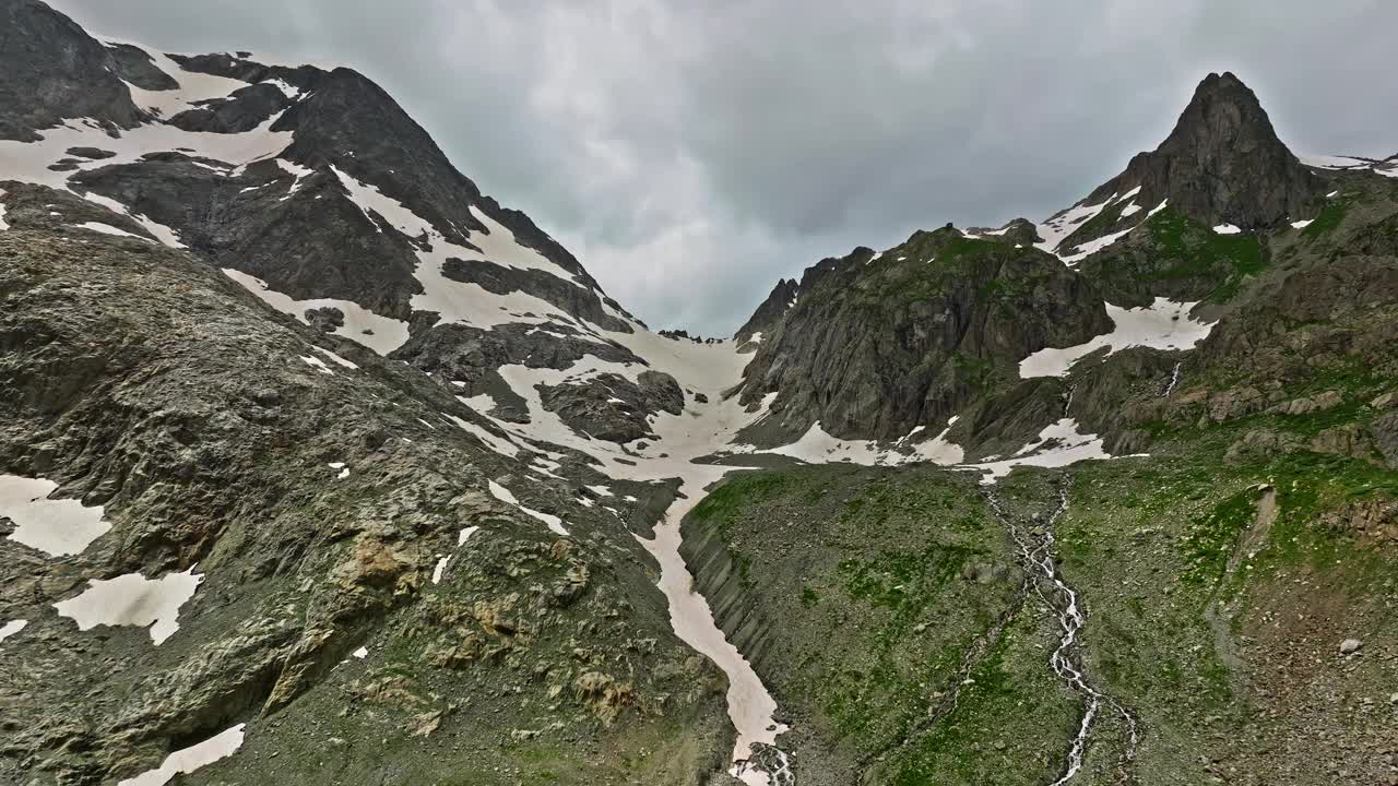 高山间古老的雪冰川。山顶上覆盖着雪。瑞士阿尔卑斯山的多山地形。无人机慢慢飞向山上几乎融化的冰川视频下载