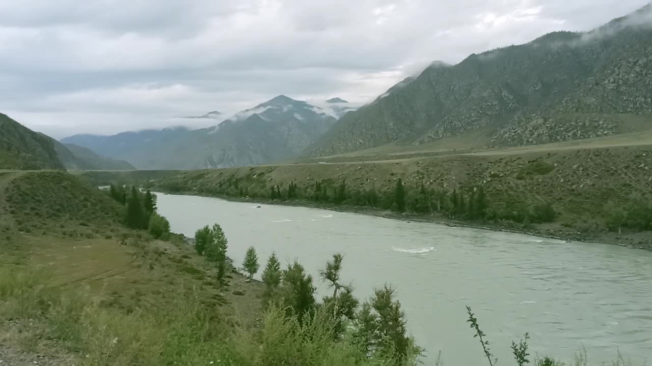 夏天的一天，一条绿松石色的宽阔河流流经一个风景如画的山谷，山谷周围群山环绕，上方正聚集着雷暴锋。视频下载