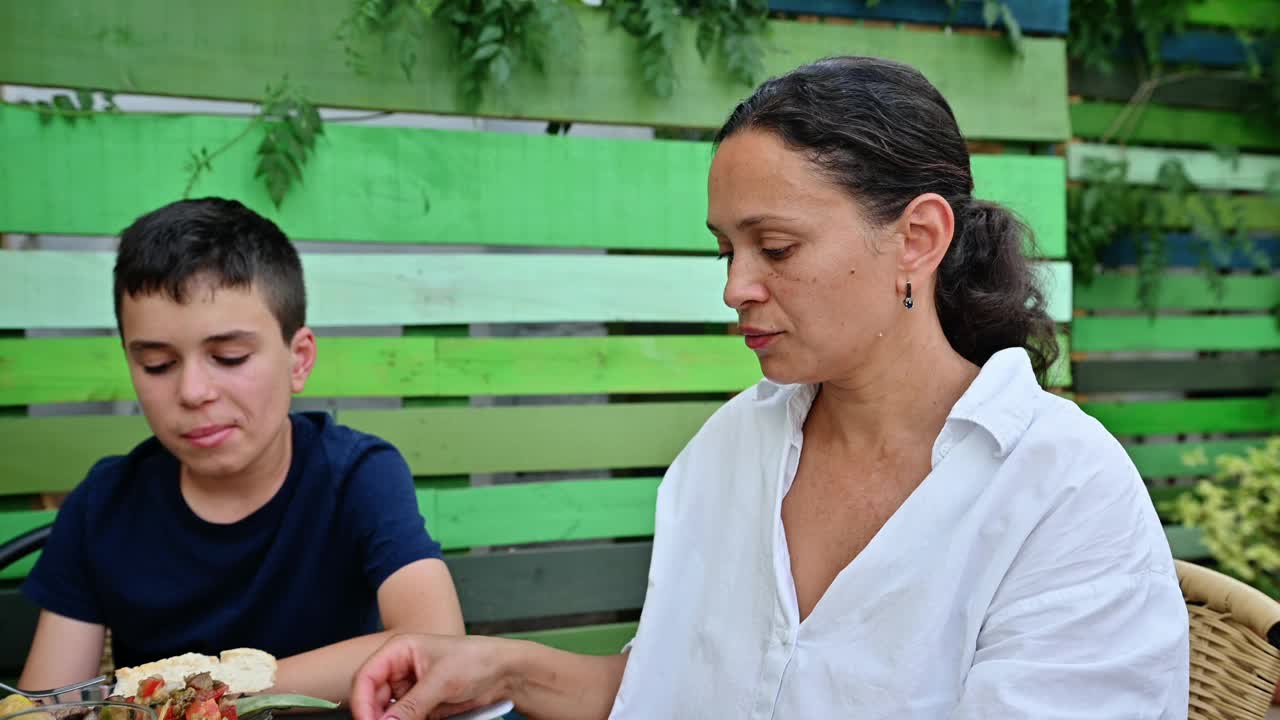 一家人在花园享受户外美食，享用健康食品。母亲和儿子在午餐时共享美好时光。视频素材