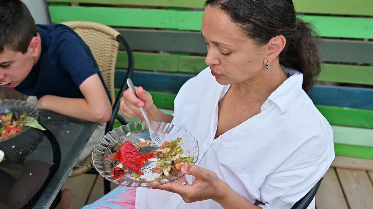 女人和小男孩在色彩缤纷的露台上享受户外用餐，在夏天的休闲家庭聚会上分享充满活力和健康的新鲜蔬菜沙拉。视频素材