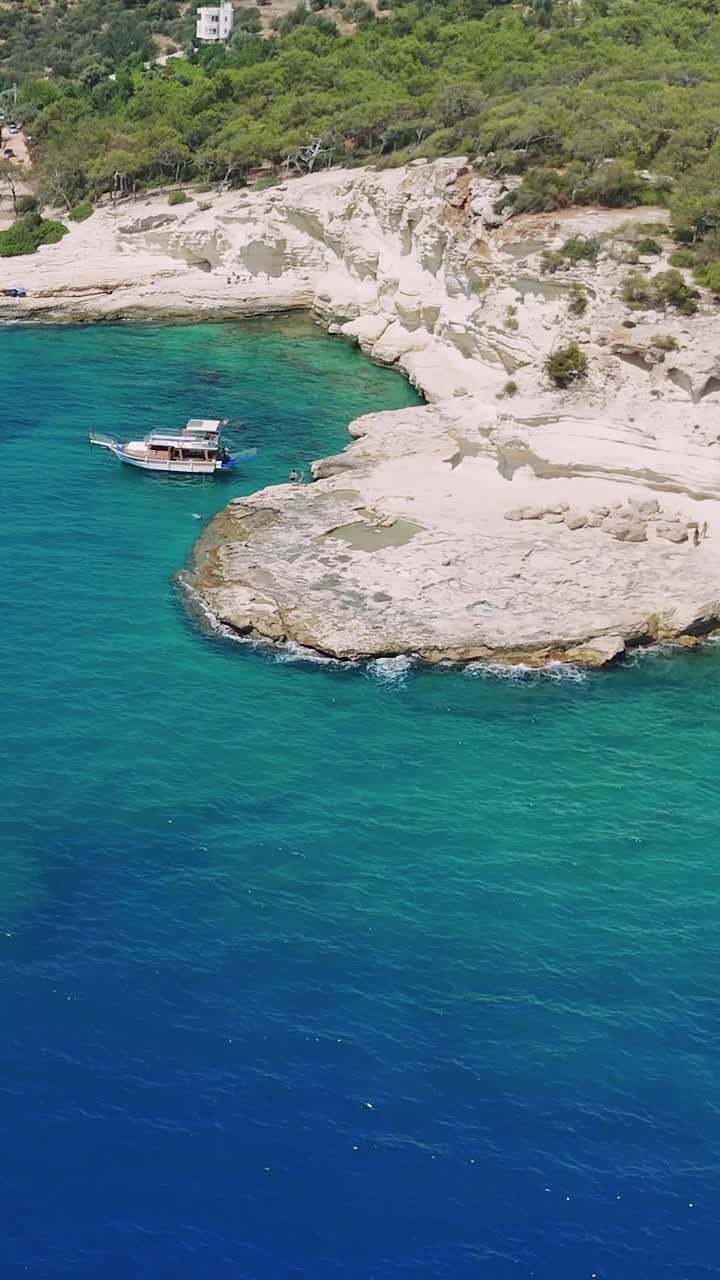 绿松石色的海浪轻轻地抚摸着崎岖的海岸线，一艘船滑向一个隐藏的海湾。郁郁葱葱的绿色植物覆盖着海岸，创造了一个宁静而令人惊叹的景观视频下载