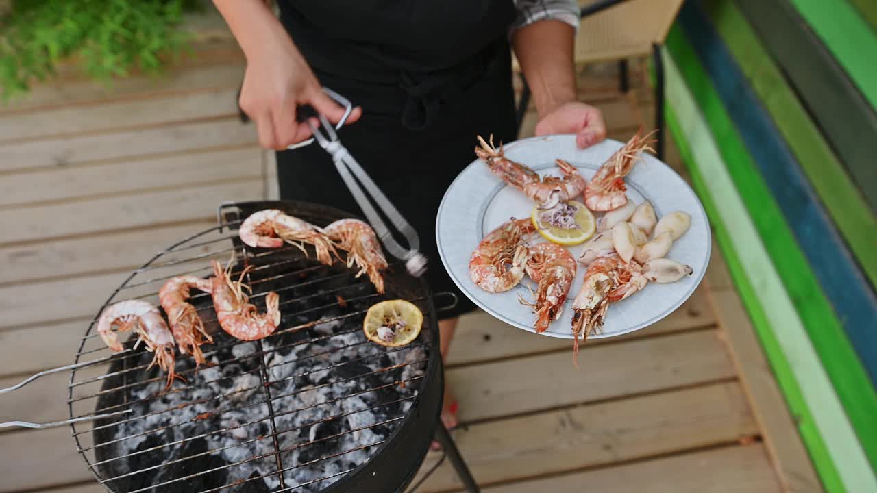 人在户外烧烤海鲜，准备美味的虾和鱿鱼烧烤。夏季烹饪经验，烧烤海鲜和充满活力的味道。视频素材