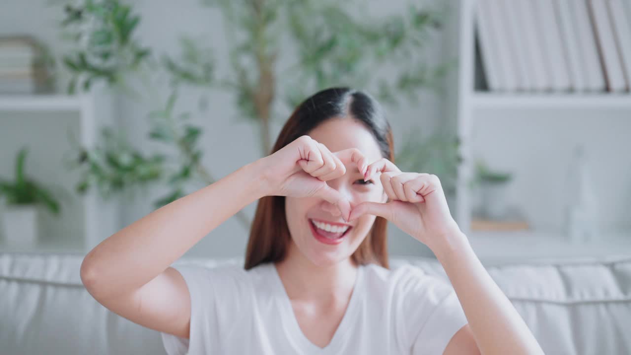 可爱的年轻亚洲女子正对着镜头微笑，双手呈心形。面部表情和积极的情绪，健康的生活，爱和慈善视频下载